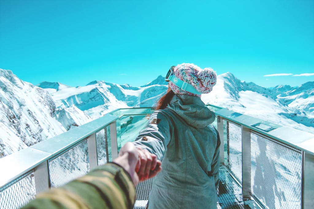 Serlig A woman in winter clothing holds a hand and walks on a scenic snow-covered mountain deck in Zell am See.