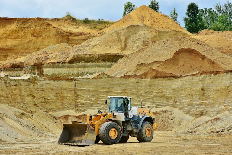 ksözcü An excavator working in an open pit mine surrounded by sandy terrain and clear sky.