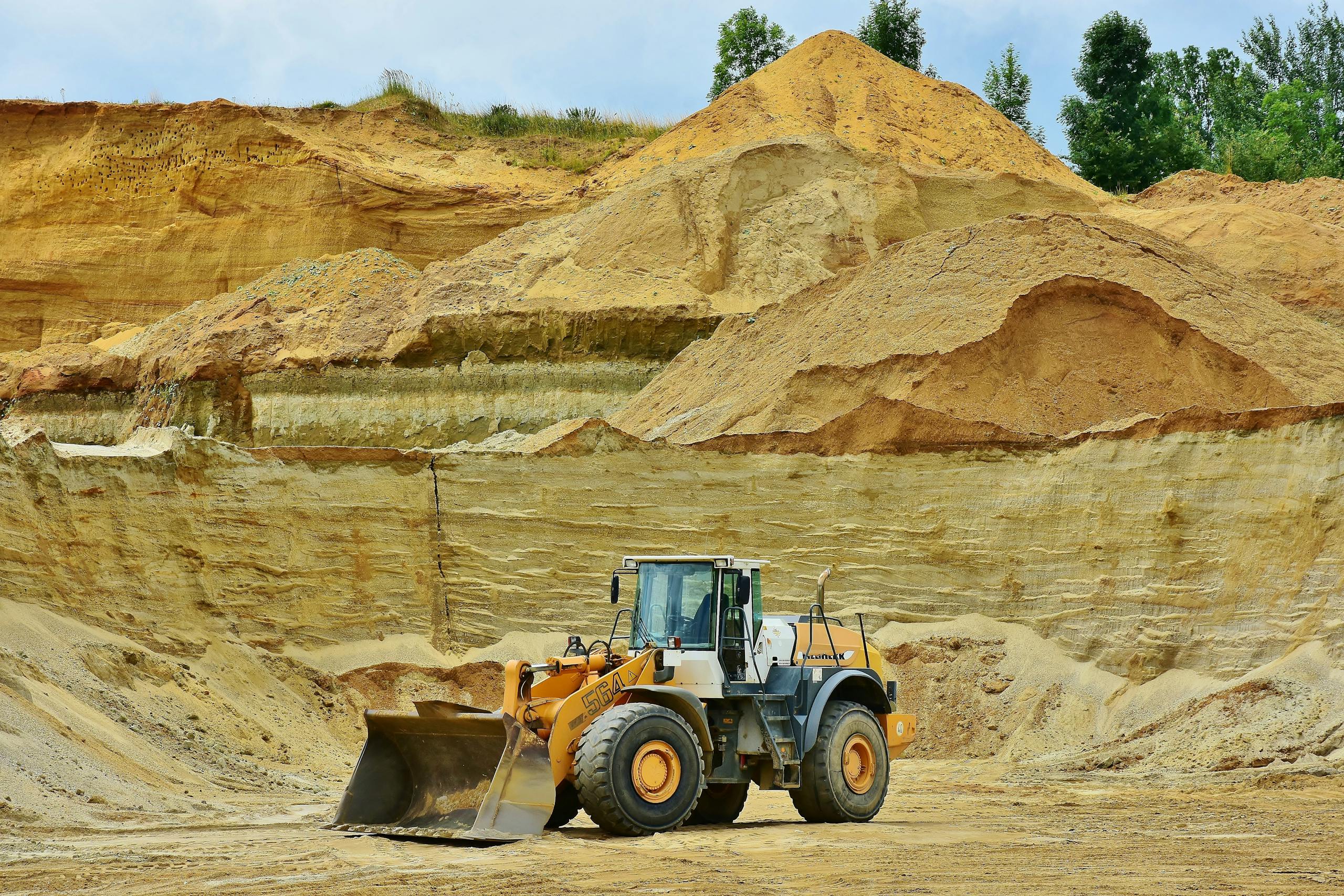 ksözcü An excavator working in an open pit mine surrounded by sandy terrain and clear sky.