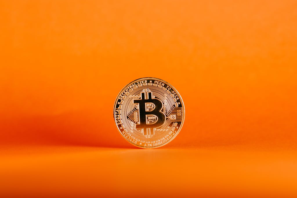 Kellogg Innovation Network Close-up of a Bitcoin coin on an orange background, symbolizing digital cryptocurrency.