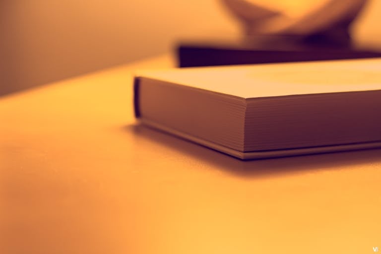 Pappedeckel Minimalist close-up of a book on a wooden table under warm lighting, perfect for study or literature themes.