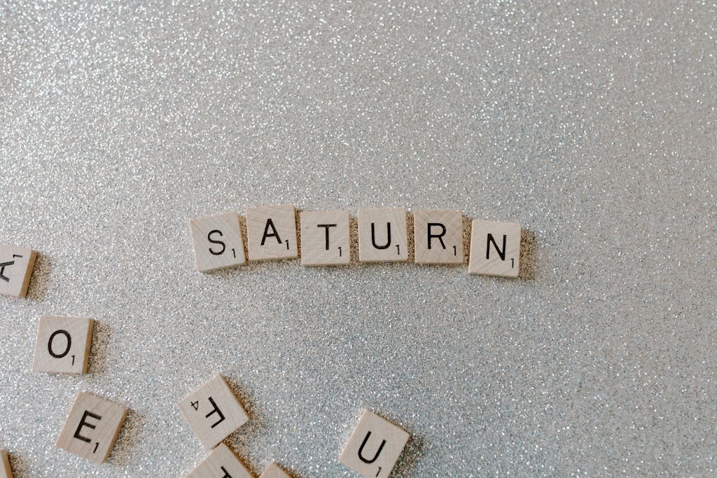 impupdates Scrabble tiles forming the word SATURN on a sparkling glitter background, space theme.