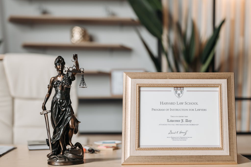Six Sigma Certification Online A framed Harvard Law School certificate beside a Lady Justice statue on an office desk.
