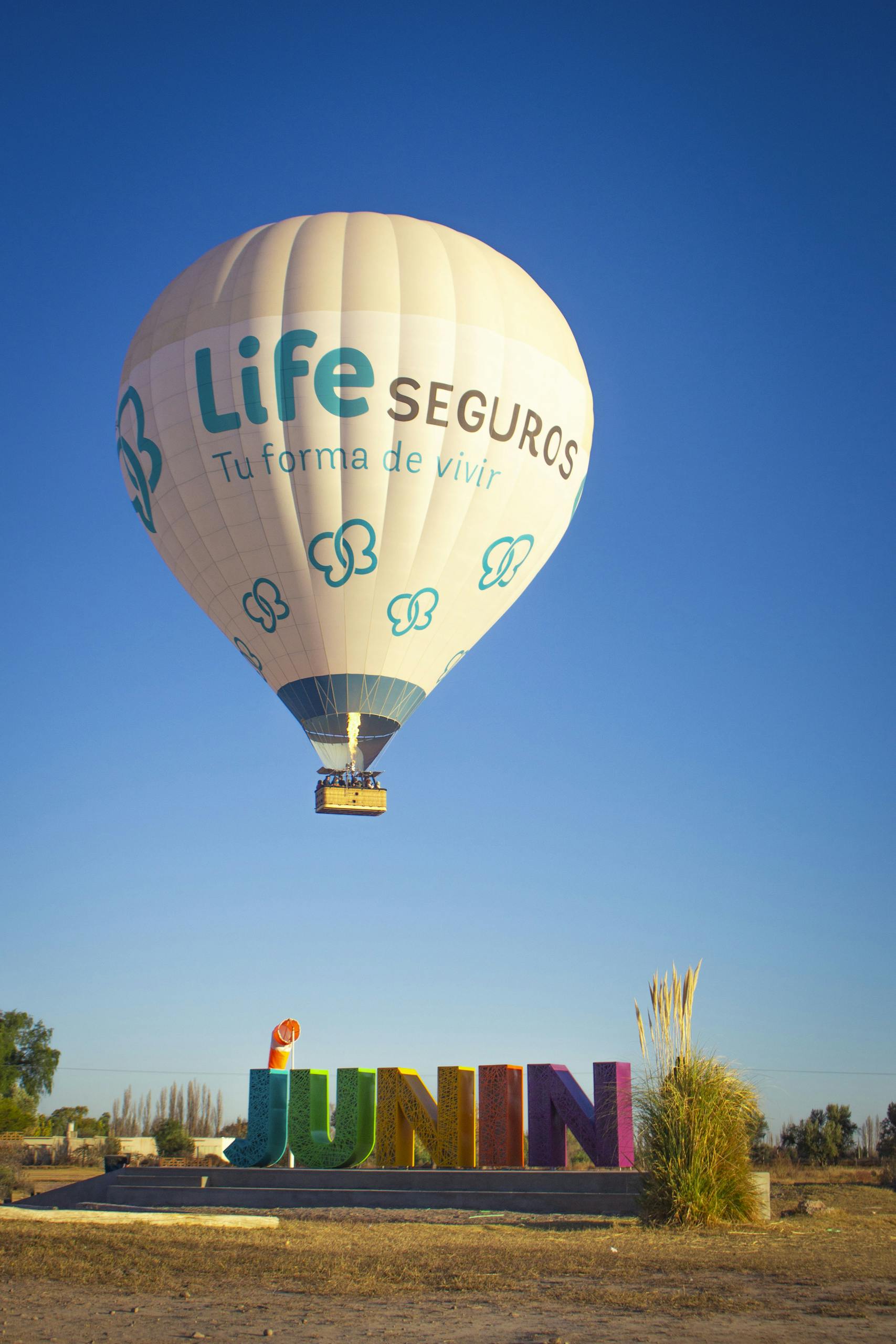 Juntos Seguros ICE A hot air balloon flying over Junín, Mendoza, against a clear blue sky.