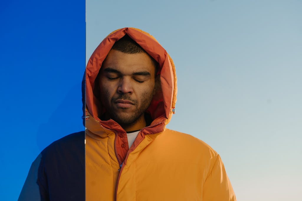 SODICERAM Juntos Seguros A man in an orange winter jacket with closed eyes stands calmly against a blue sky.