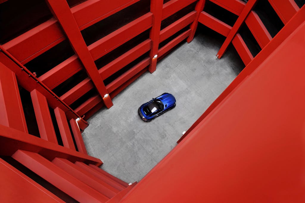 123safe67  A striking image of a blue car parked in a vibrant red parking structure, captured from above.