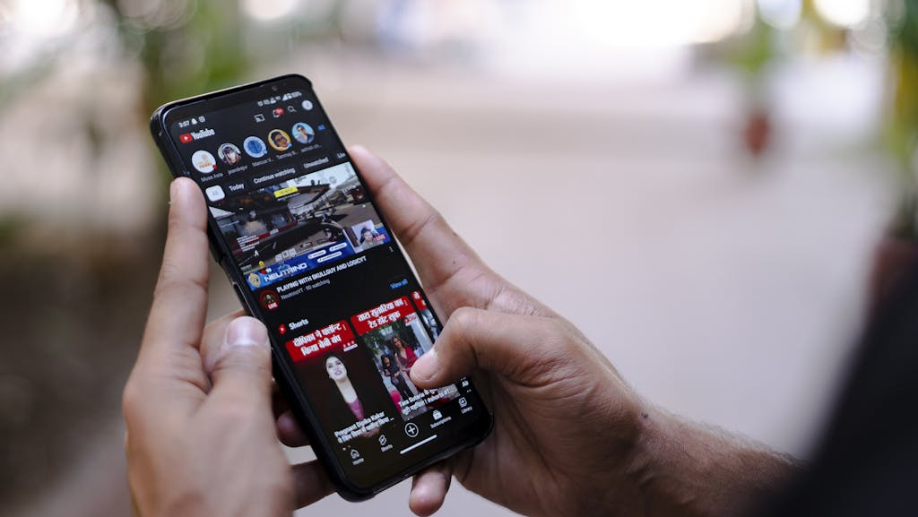  ibomma1.com  Close-up of hands using a smartphone to watch YouTube outdoors, showcasing digital connectivity.