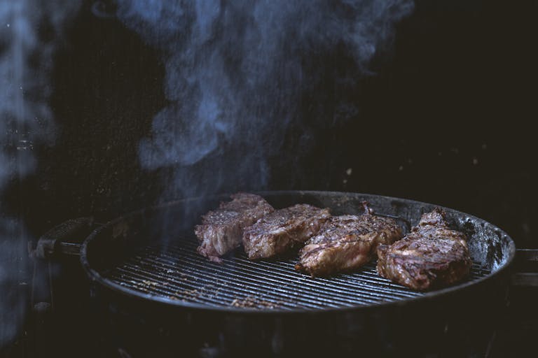 Weber Grillvorführung Close-up of juicy steaks grilling on a smoky barbecue, perfect for summer cookouts.