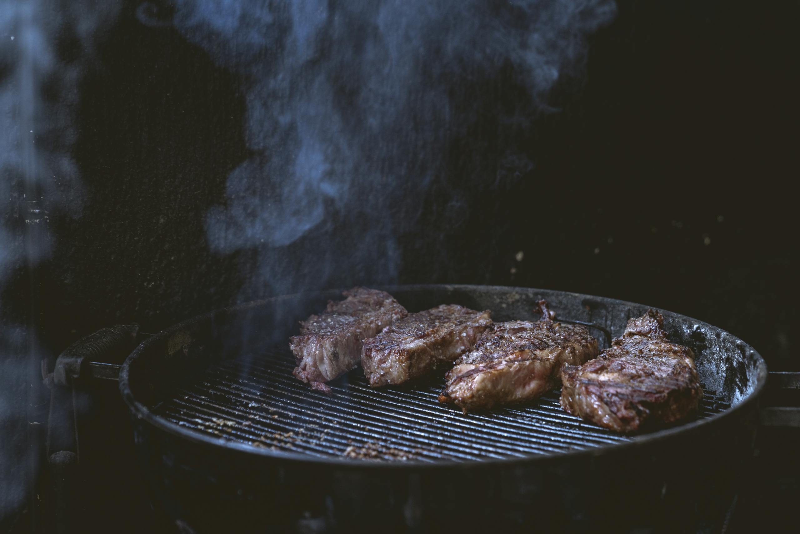 Weber Grillvorführung Close-up of juicy steaks grilling on a smoky barbecue, perfect for summer cookouts.