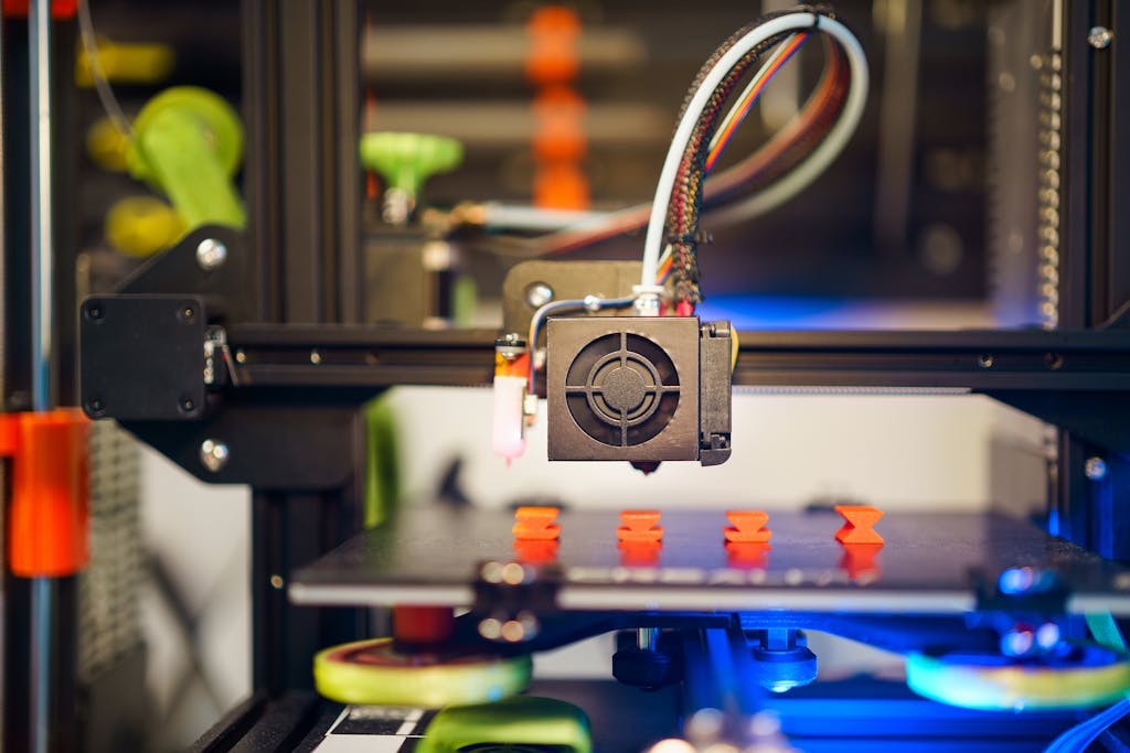 uitly.blog Detailed view of a 3D printer in action, fabricating small plastic pieces indoors.