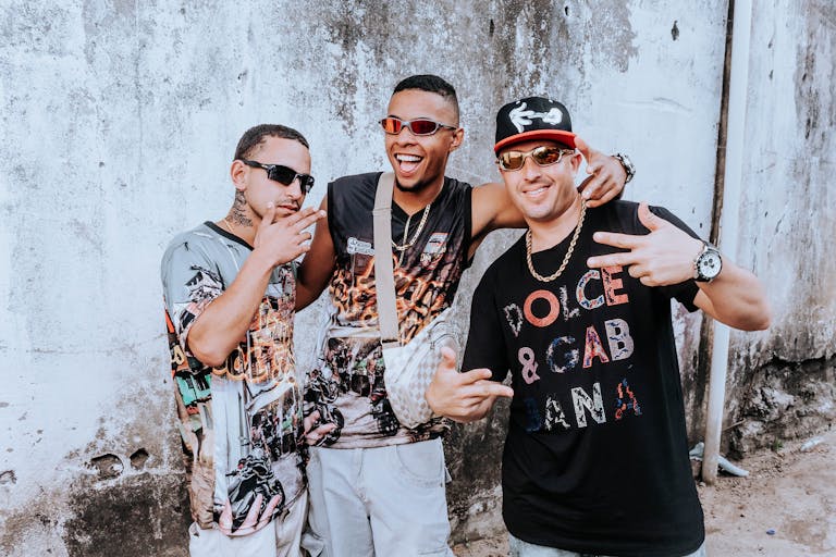 MC Lyte Three urban musicians posing energetically against a rustic wall, showcasing streetwear fashion.